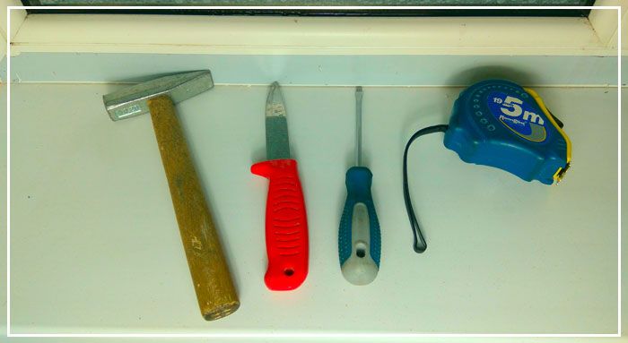 Нож, отвертка, молоток и рулетка на пластиковом подоконнике