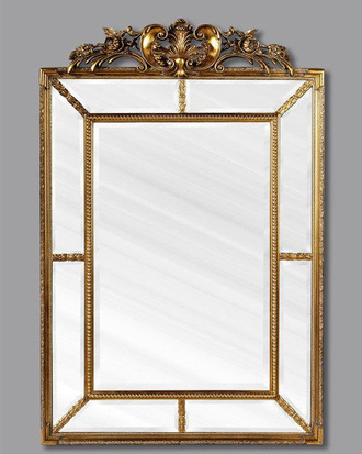 Зеркало в золотой раме в стиле “барокко” с цветочным орнаментом сверху.