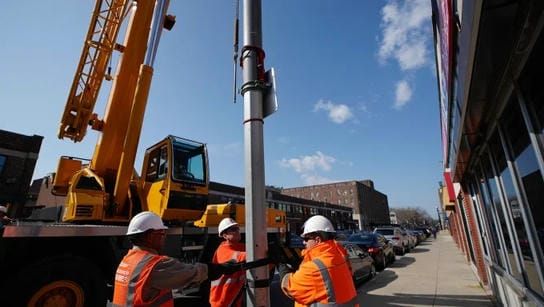 Процесс демонтажа высокой стальной опоры освещения с использованием автокрана в городе.
