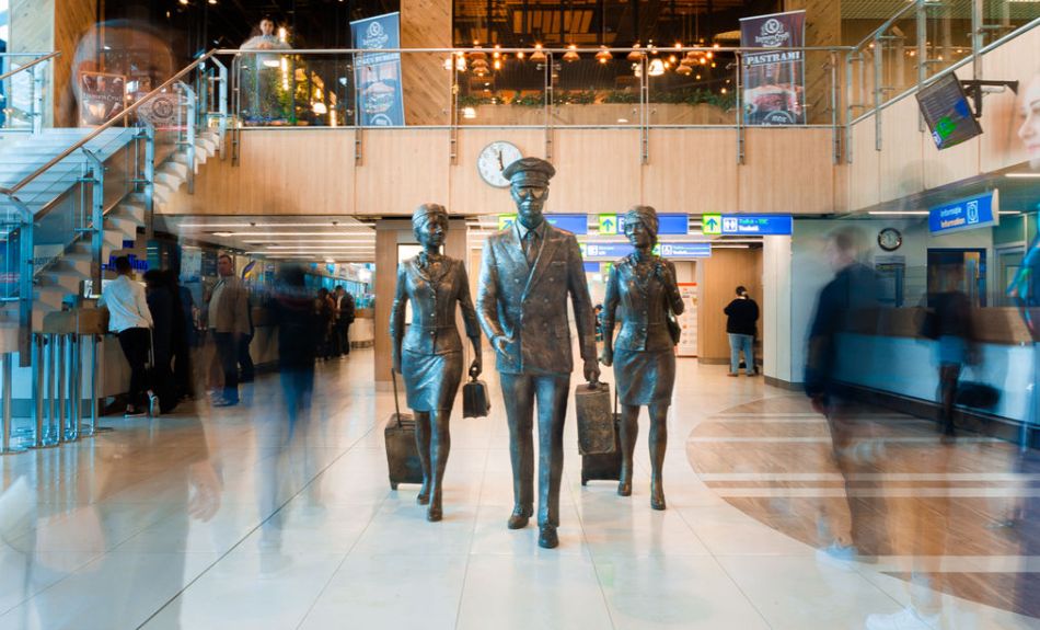 На изображении интерьер зала отправления аэропорта Кишинева с монументом спешащих пилота, стюардесс.