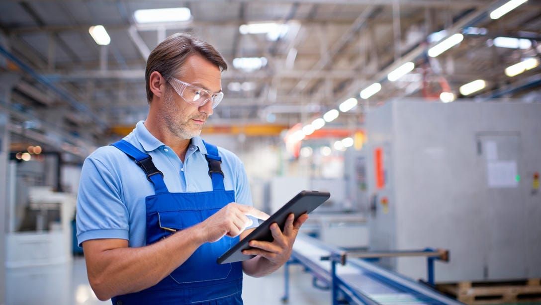 Инженер с планшетом проверяет показатели энергопотребления и графики на фоне промышленных светильник