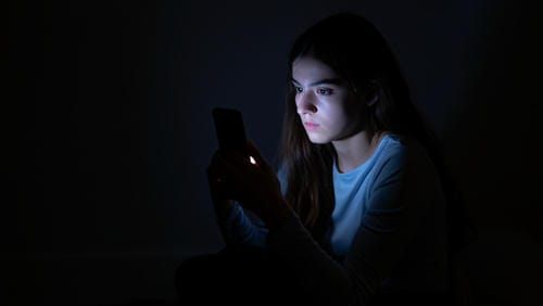Женщина смотрит на светящийся экран телефона в темной комнате