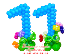 Плетеные цифры 11 из шаров голубого цвета на цветочных клумбах