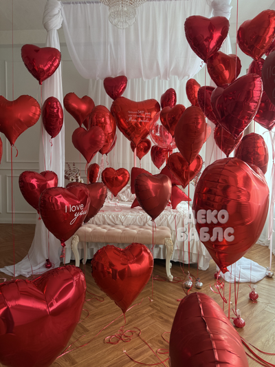 Праздничное оформление интерьера спальни множеством красных гелиевых шаров в форме сердец Троицк Нов