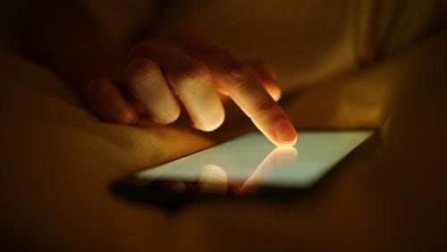 Рука касается экрана смартфона, от которого исходит мягкое, успокаивающее сияние.