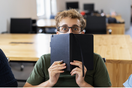 мальчик в очках и зеленой футболке прячет лицо за записной книжкой