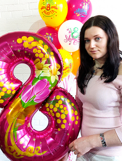 Девушка с шариком в форме цифры 8, но фоне гелиевые шарики с рисунком "8 марта"