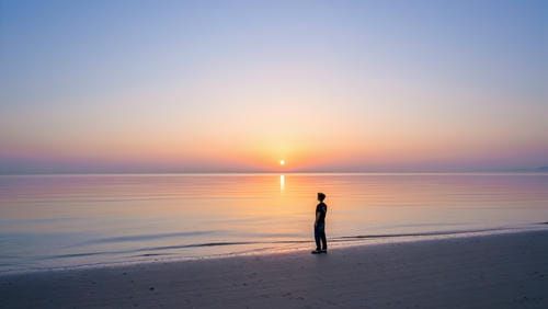 Человек стоит на берегу моря на рассвете, символизируя чистоту и новое начало.
