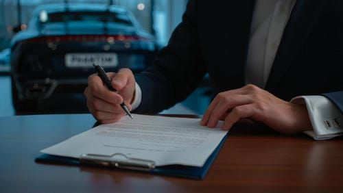 Мужчина в деловом костюме внимательно изучает договор аренды автомобиля представительского класса