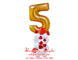Золотая фольгированная цифра 5 на белом подиуме из шаров с красными сердечками