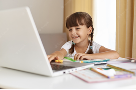 Счастливая девочка с косичками сидит перед ноутбуком улыбается
