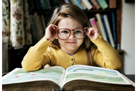 Счастливая девочка сидит перед книгой в очках улыбается